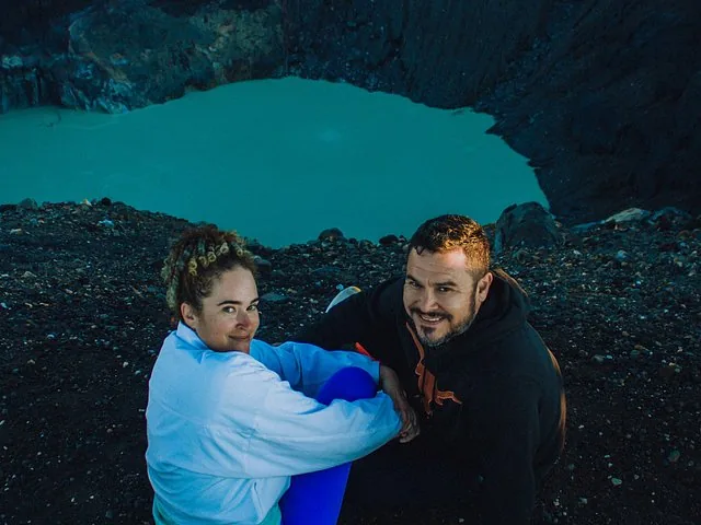 A couple poses on the dark rocky edge overlooking Santa Ana Volcano crater lake.