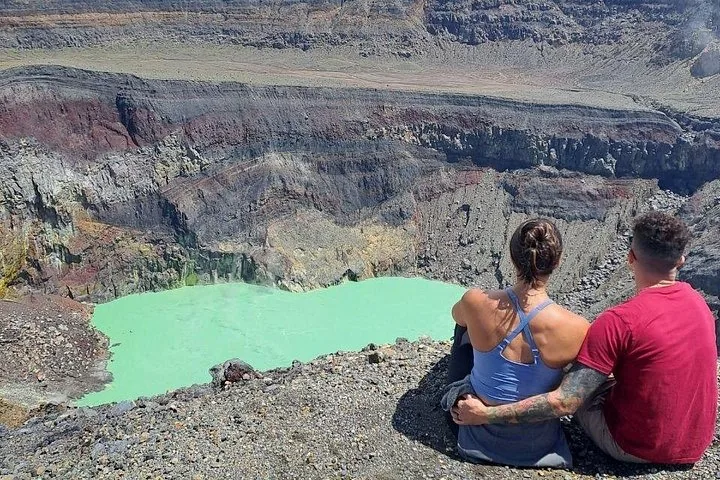 Pareja sentada en el borde de un cráter volcánico con un lago turquesa.