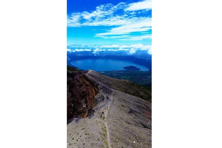 Escursionisti che camminano su una cresta vulcanica con un lago blu sullo sfondo.