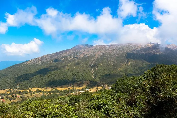 Vista panorámica de una gran montaña volcánica verde parcialmente cubierta por nubes